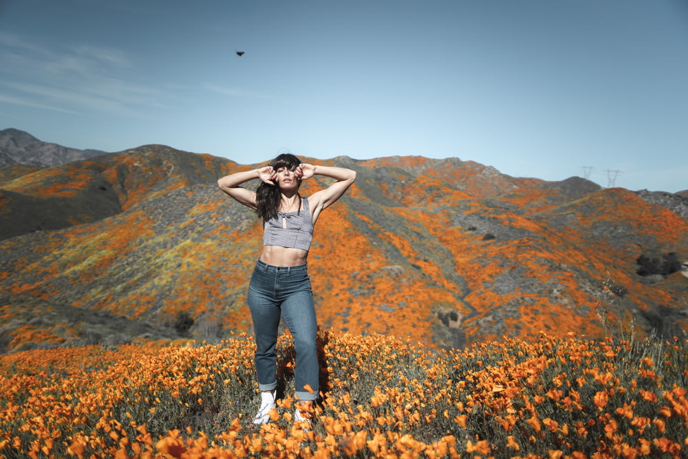 Frau in grauem Crop-Top und Jeans-Unterteil steht in der Nähe eines orangefarbenen Blumenfeldes