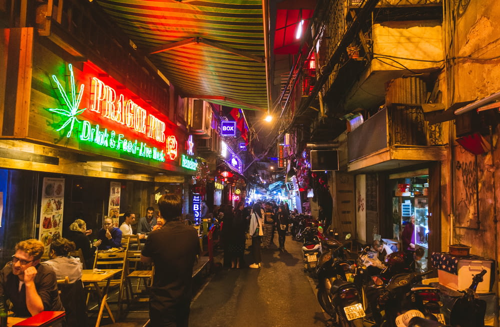 people walking and sitting beside buildings near busy street during night time