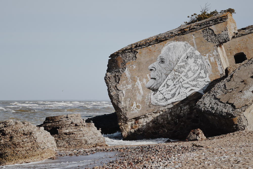 white woman with shawl drawing on concrete block in beach