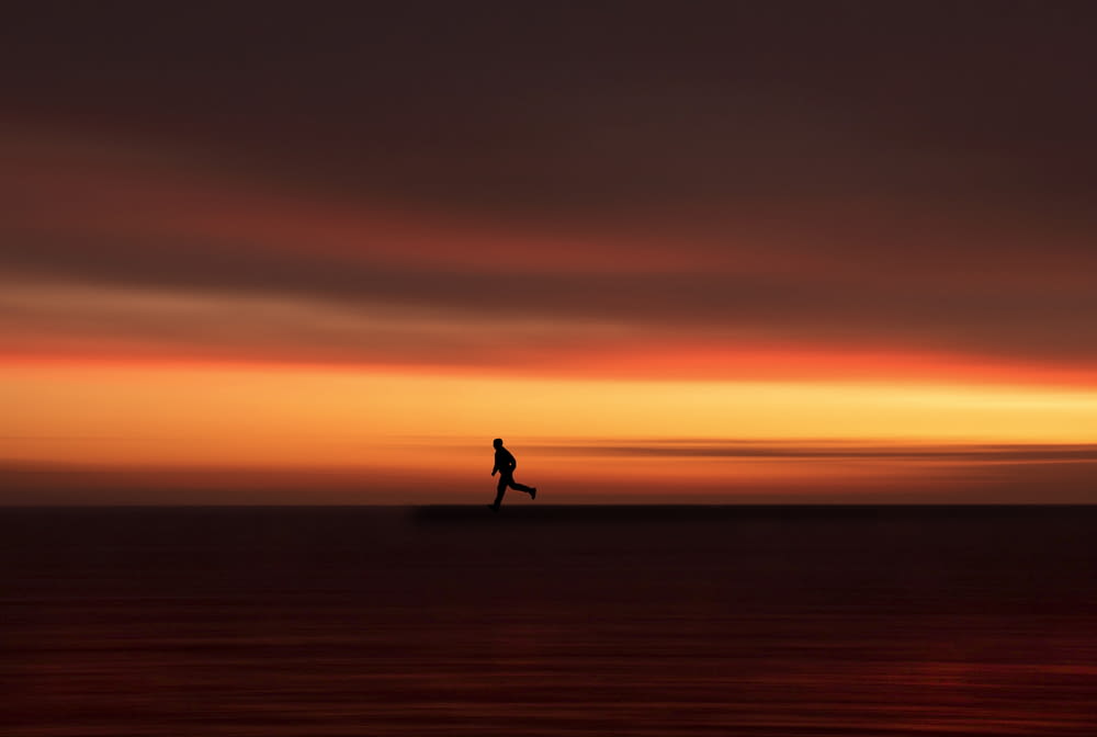 silhouette di persona che cammina sul campo durante il tramonto