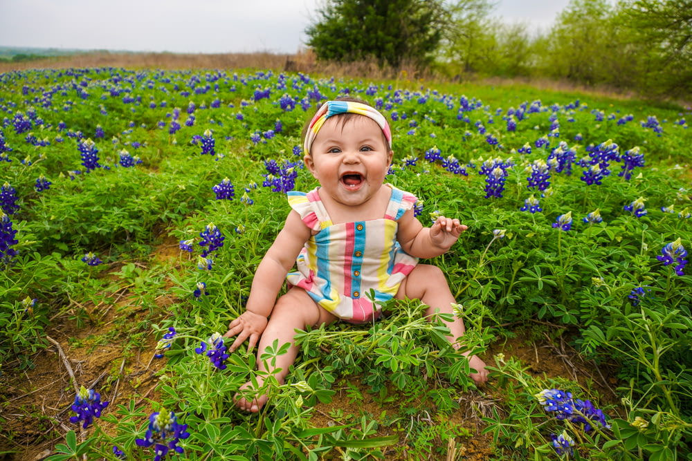 a baby sitting in a field of blue flowers