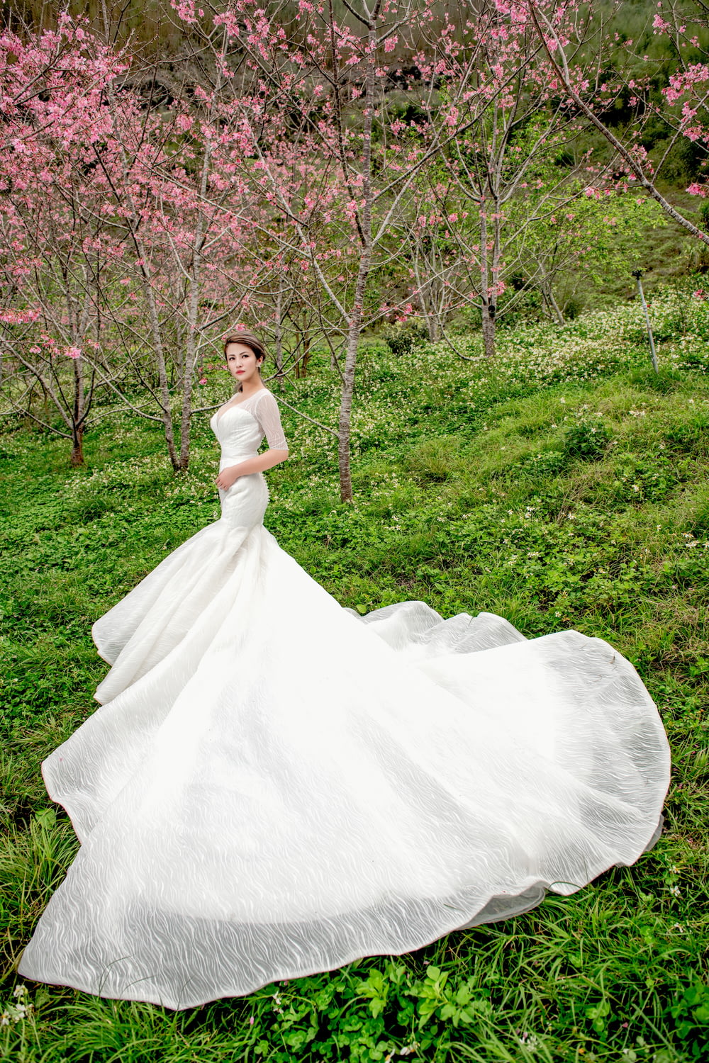 woman wearing white wedding dress standing near pink flowering trees