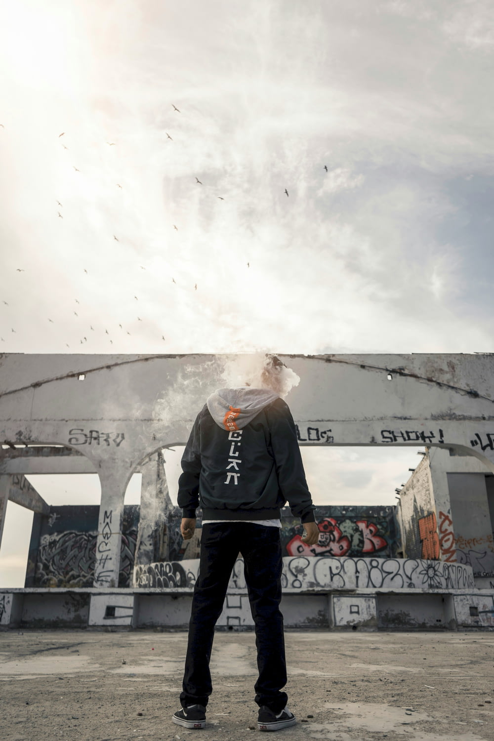 headless person in black hoodie and pants standing near concrete structure