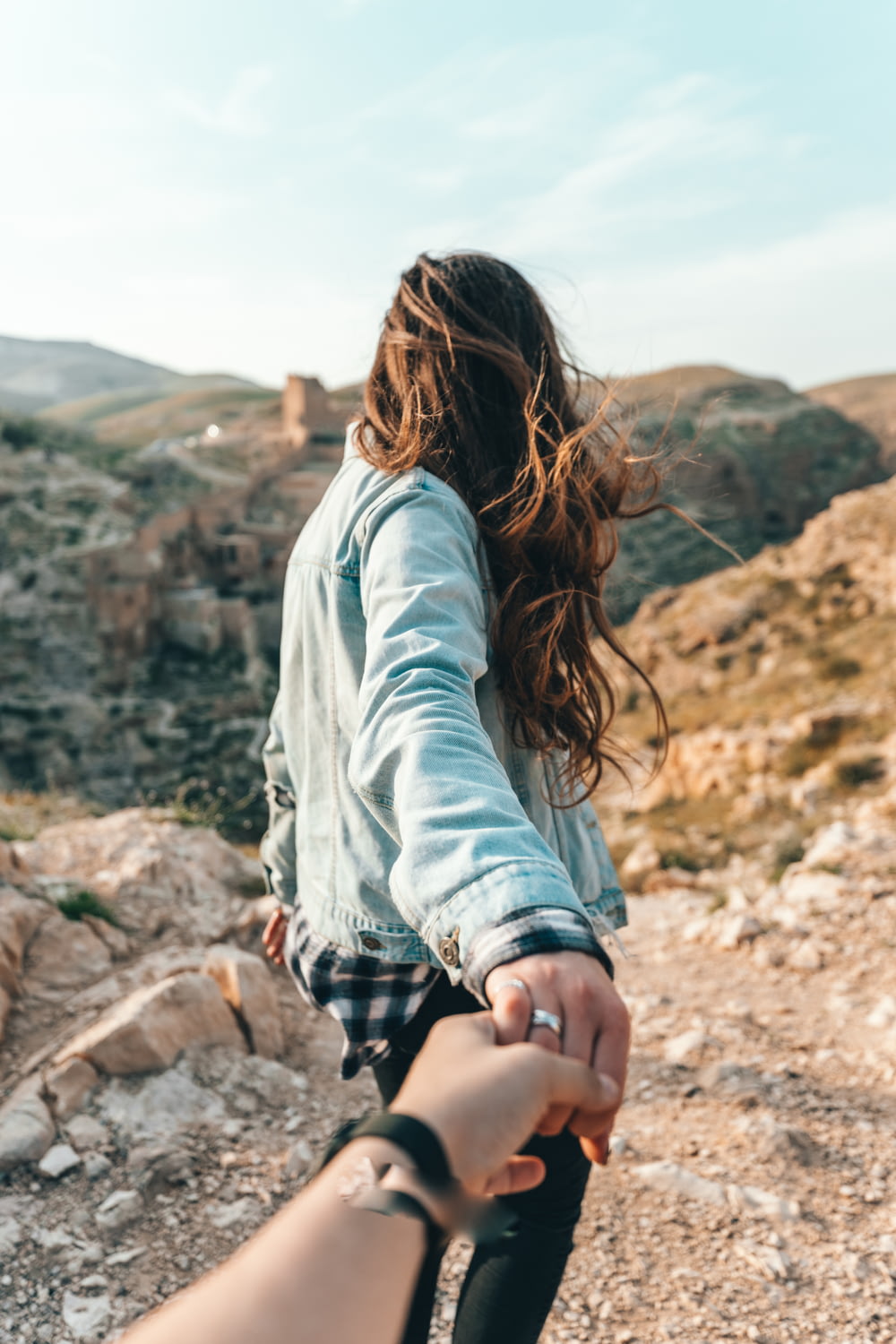 person holding hand of woman wearing gray jacket overlooking mountain during daytime
