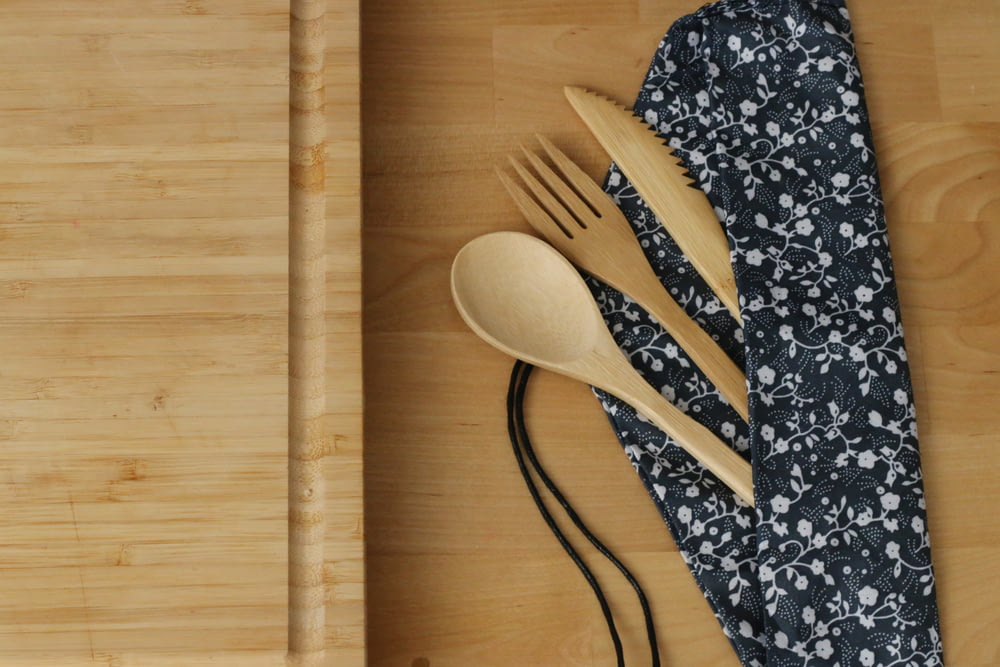a wooden spoon, fork, and knife rest on a bamboo cutting board