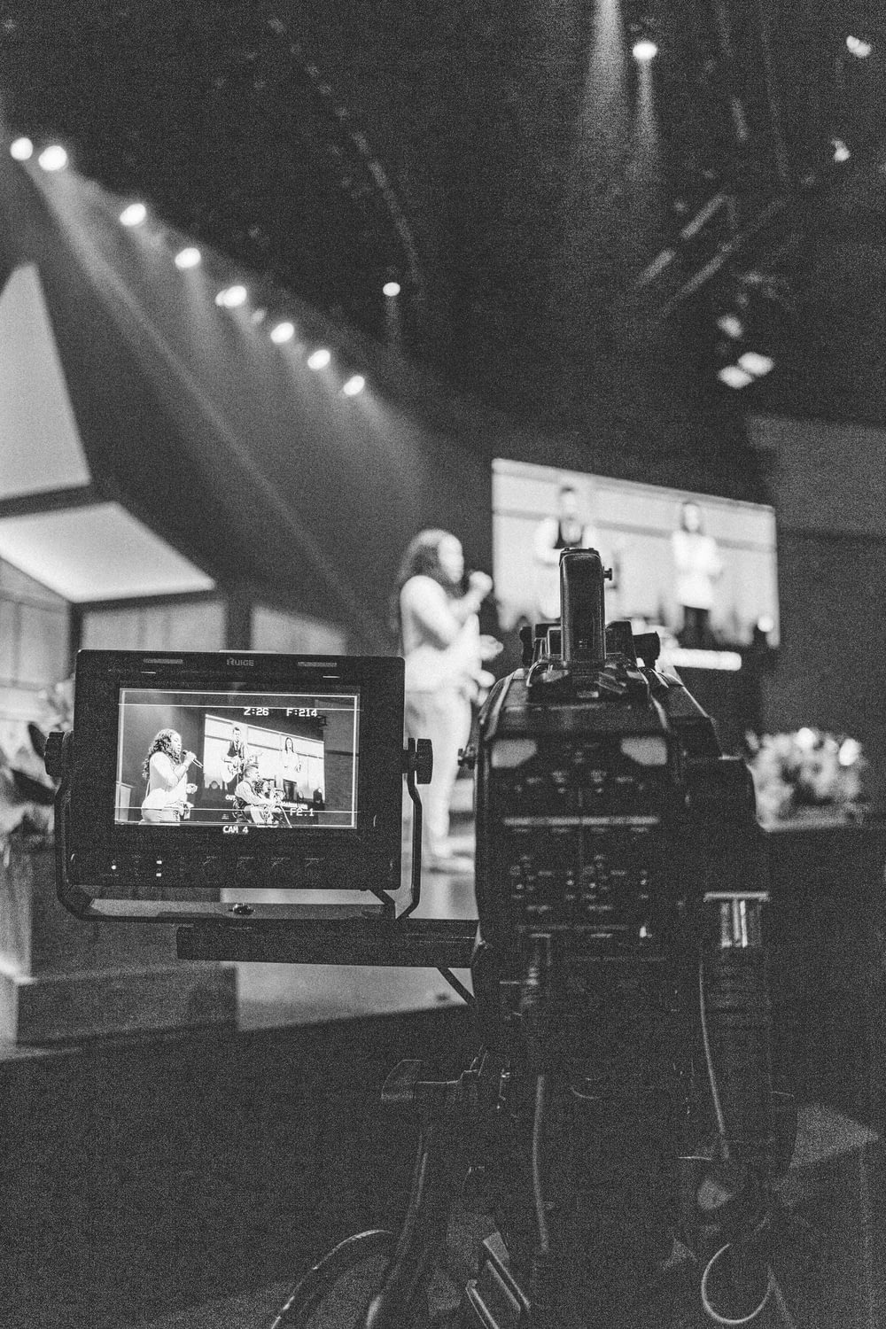 greyscale photography of video camera capturing person standing on stage