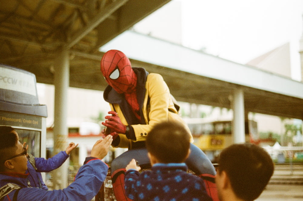 a man in a spider man costume is handing something to a child