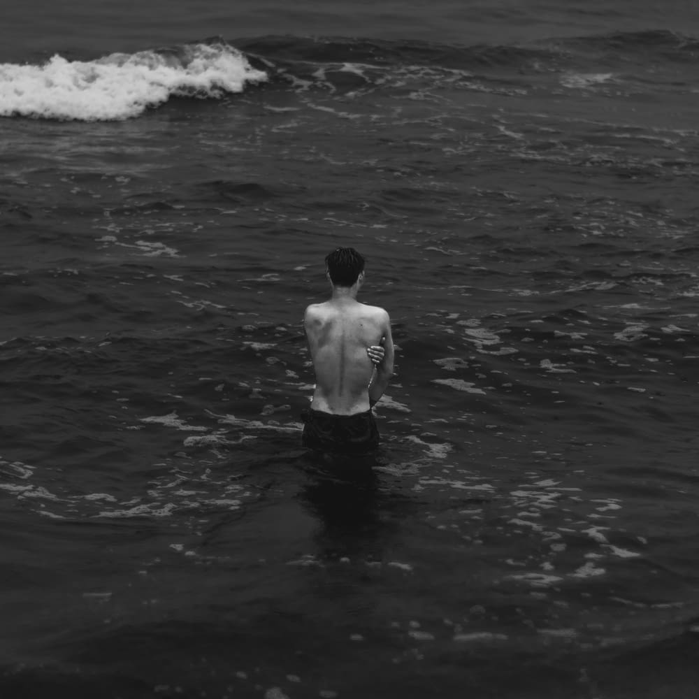 grayscale photography of man half-dipped in the sea