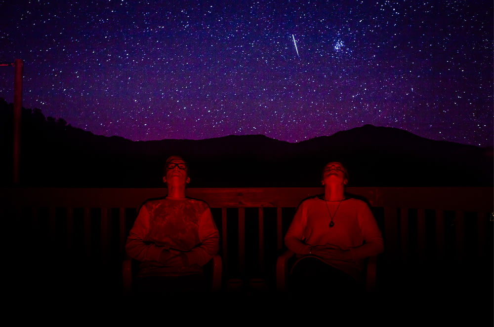 two men sitting under starry sky during nighttime