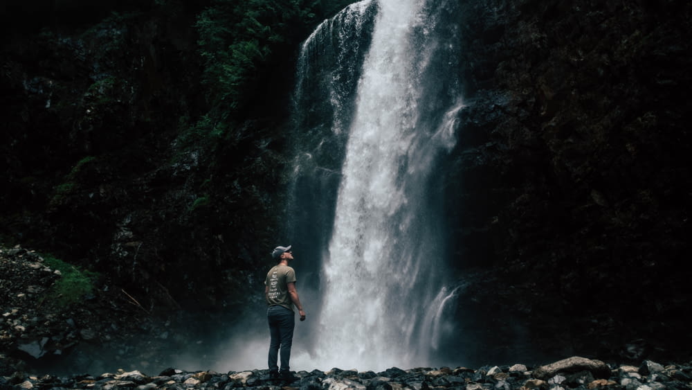 man standing in front of waterfall looking up