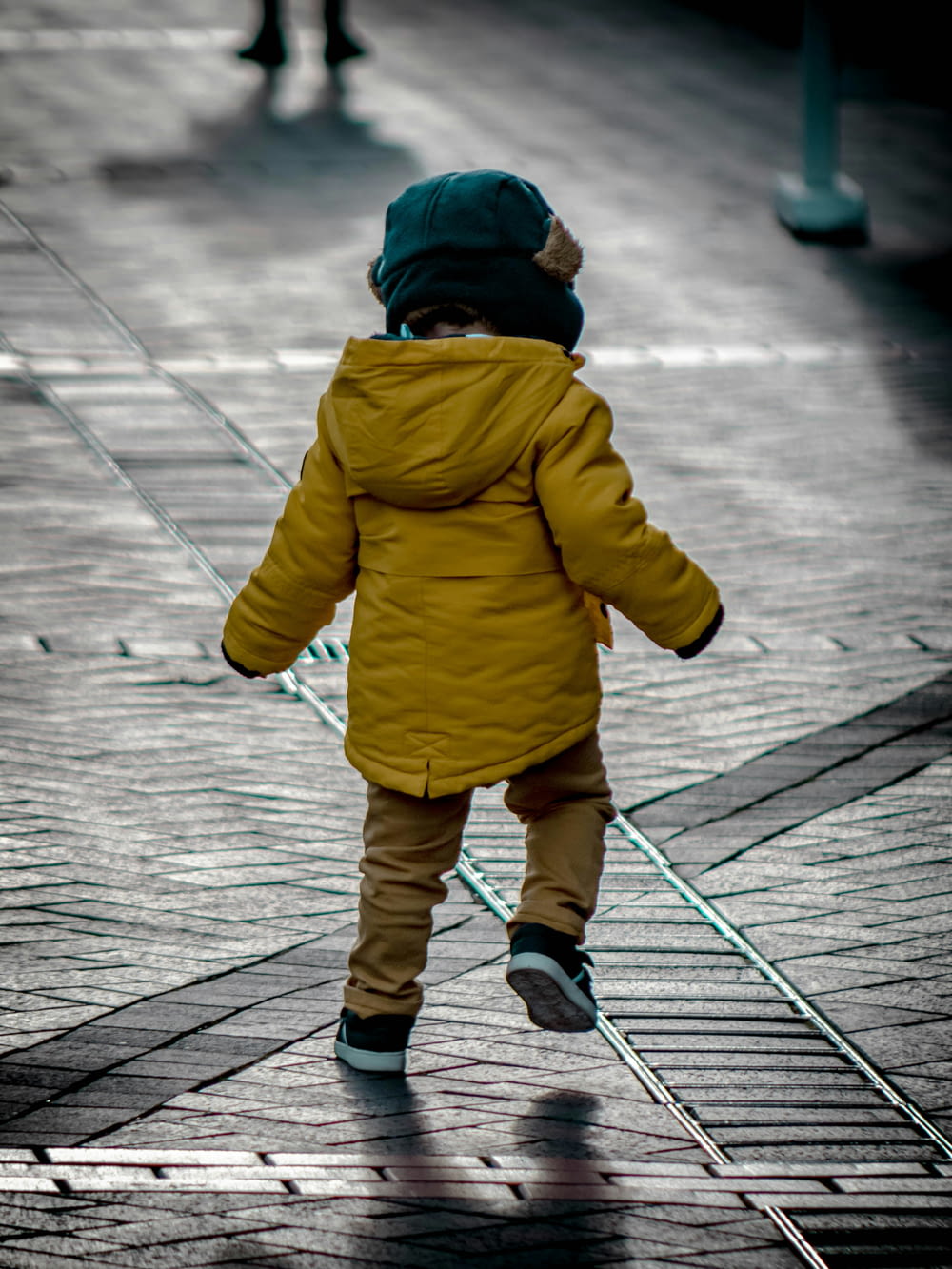 toddler wearing yellow jacket on gray concrete floor