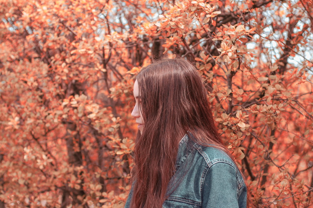 woman wearing denim jacket near orange leaf trees