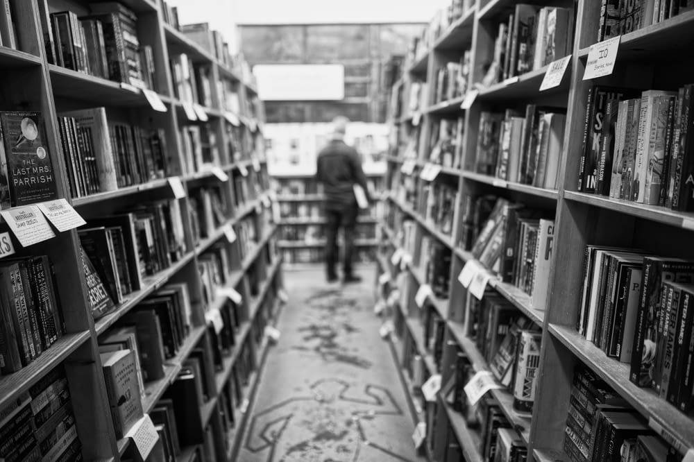 Photo en niveaux de gris d’un homme debout devant des livres