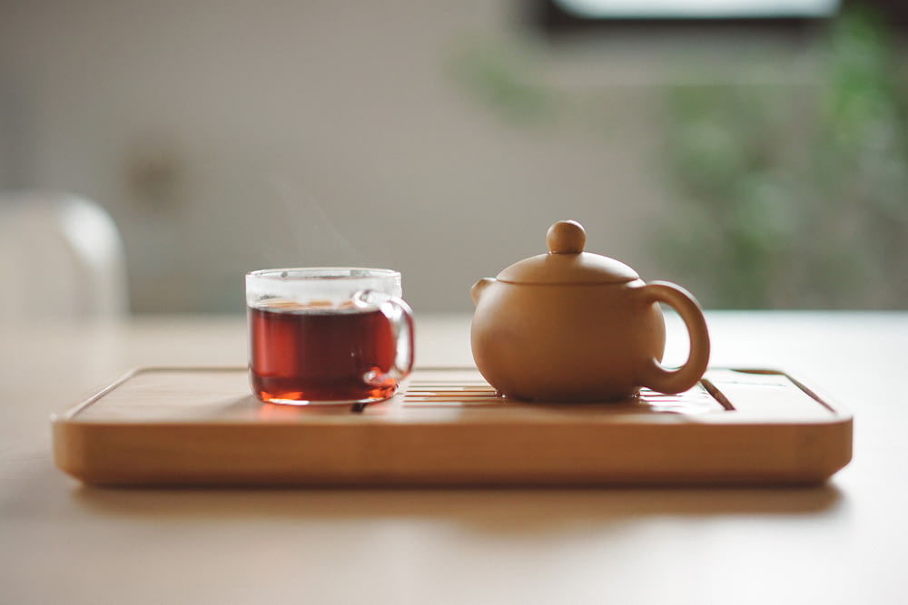 Tasse en verre transparent avec thé près de la théière en céramique brune