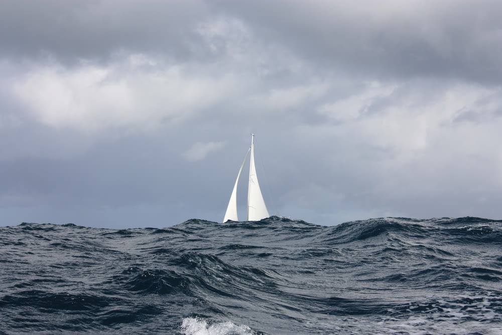 white sailing boat under nimbus clouds