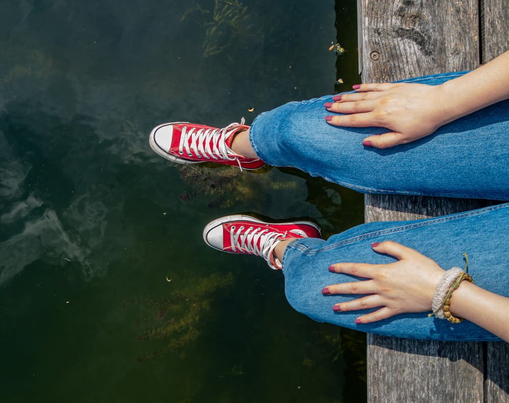 person wearing denim jeans sitting on wooden dock during daytime