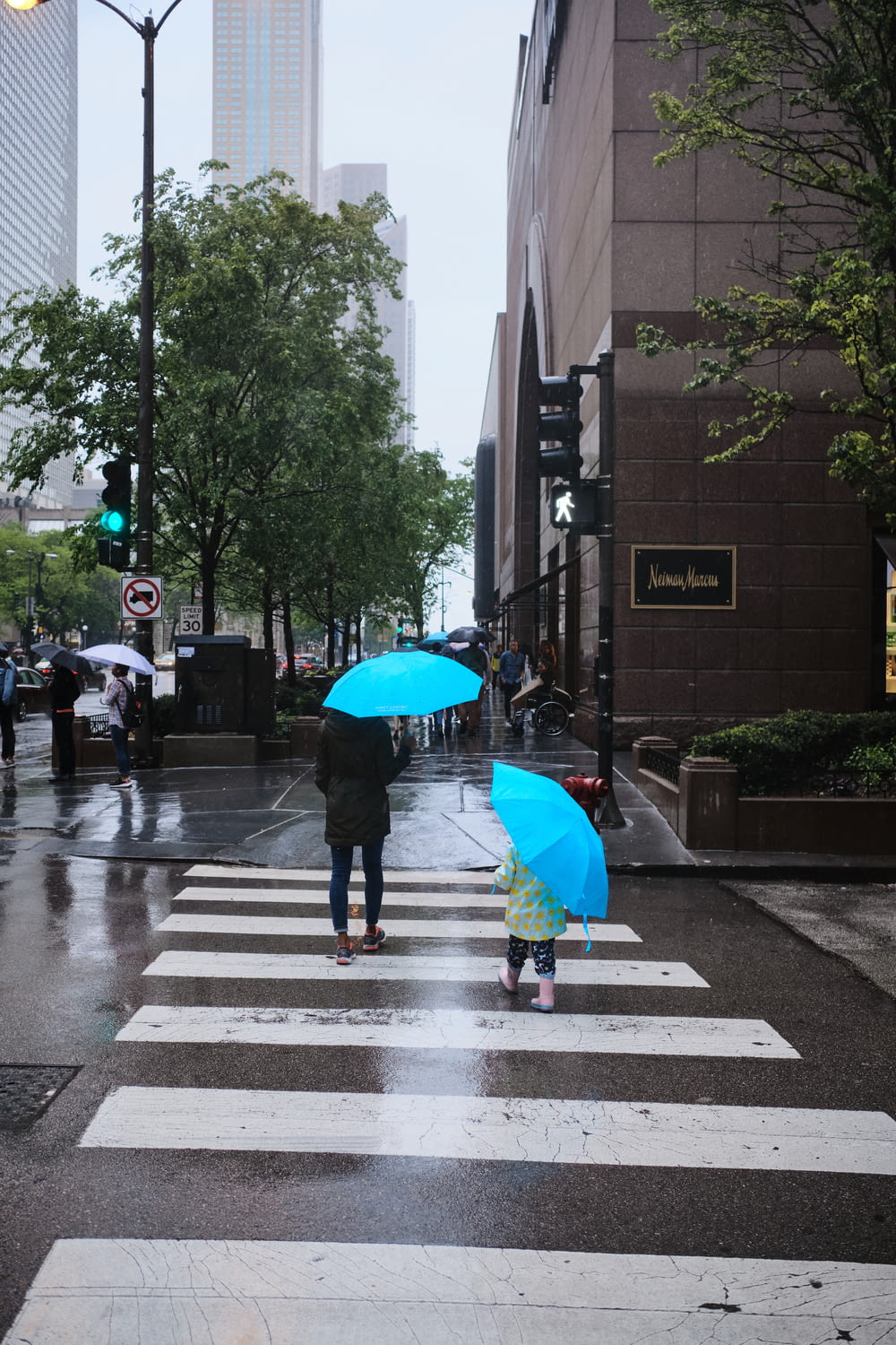 woman and girl walking on pedestrian lane while holding umbrella