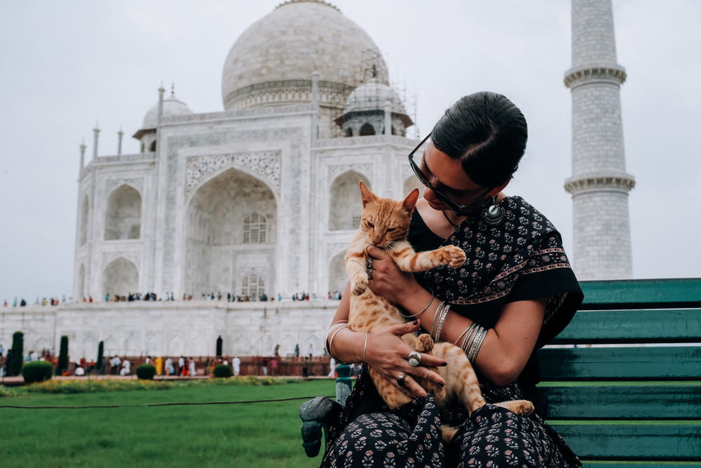 woman carrying orange tabby cat across white mosque