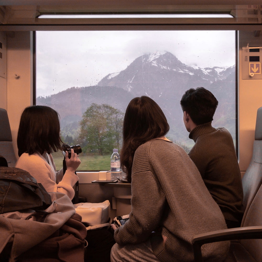 three people sitting on a train looking out the window