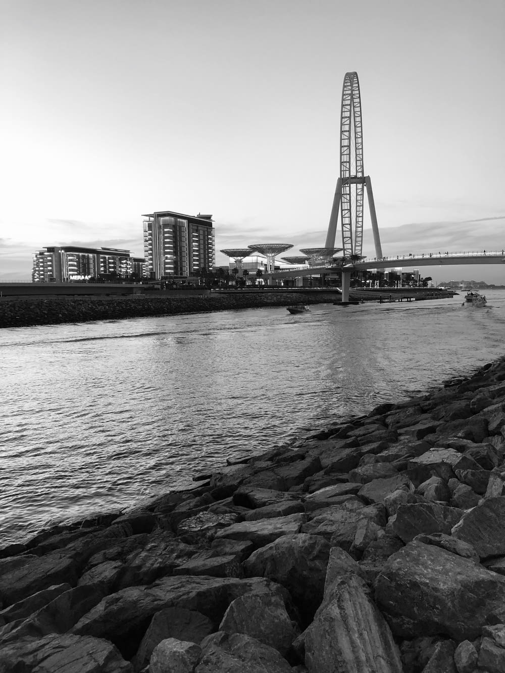 grayscale photo of body of water over bridge facing buildings