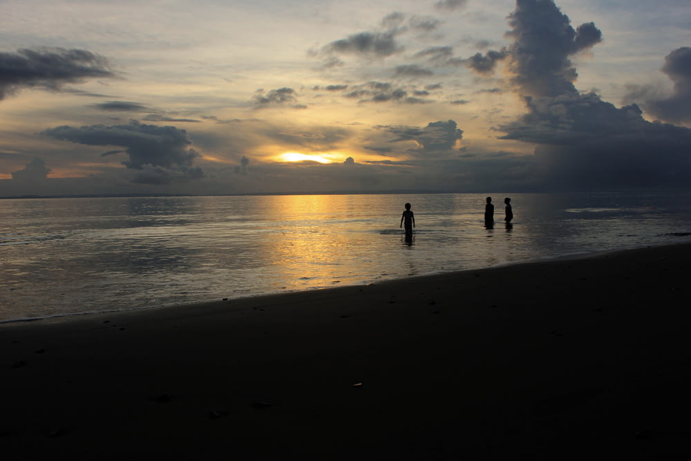 silhouette of three people near shore