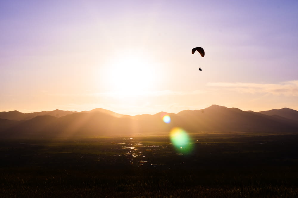 silhouette of person hanging on parachute during sunset