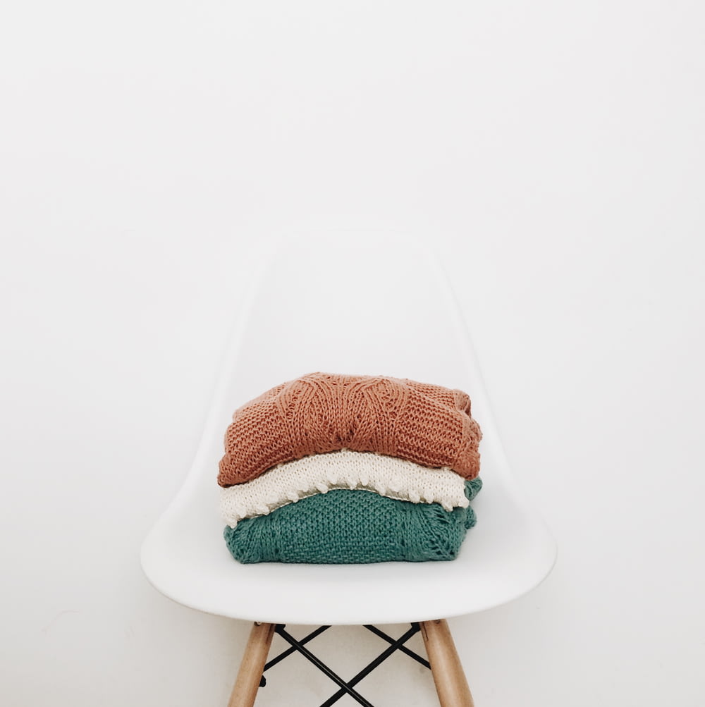 tres pilas de ropa tejida en una silla blanca