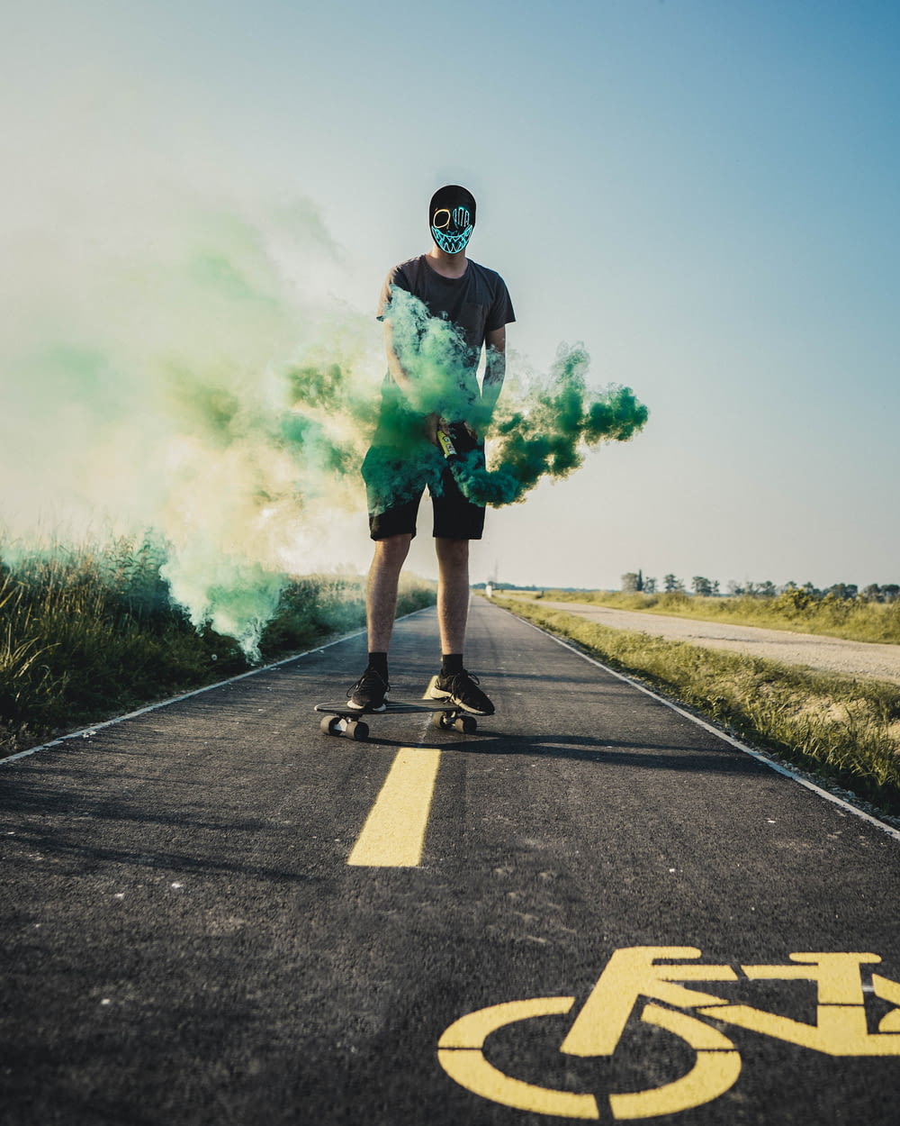man standing on gray and yellow road holding green smoke