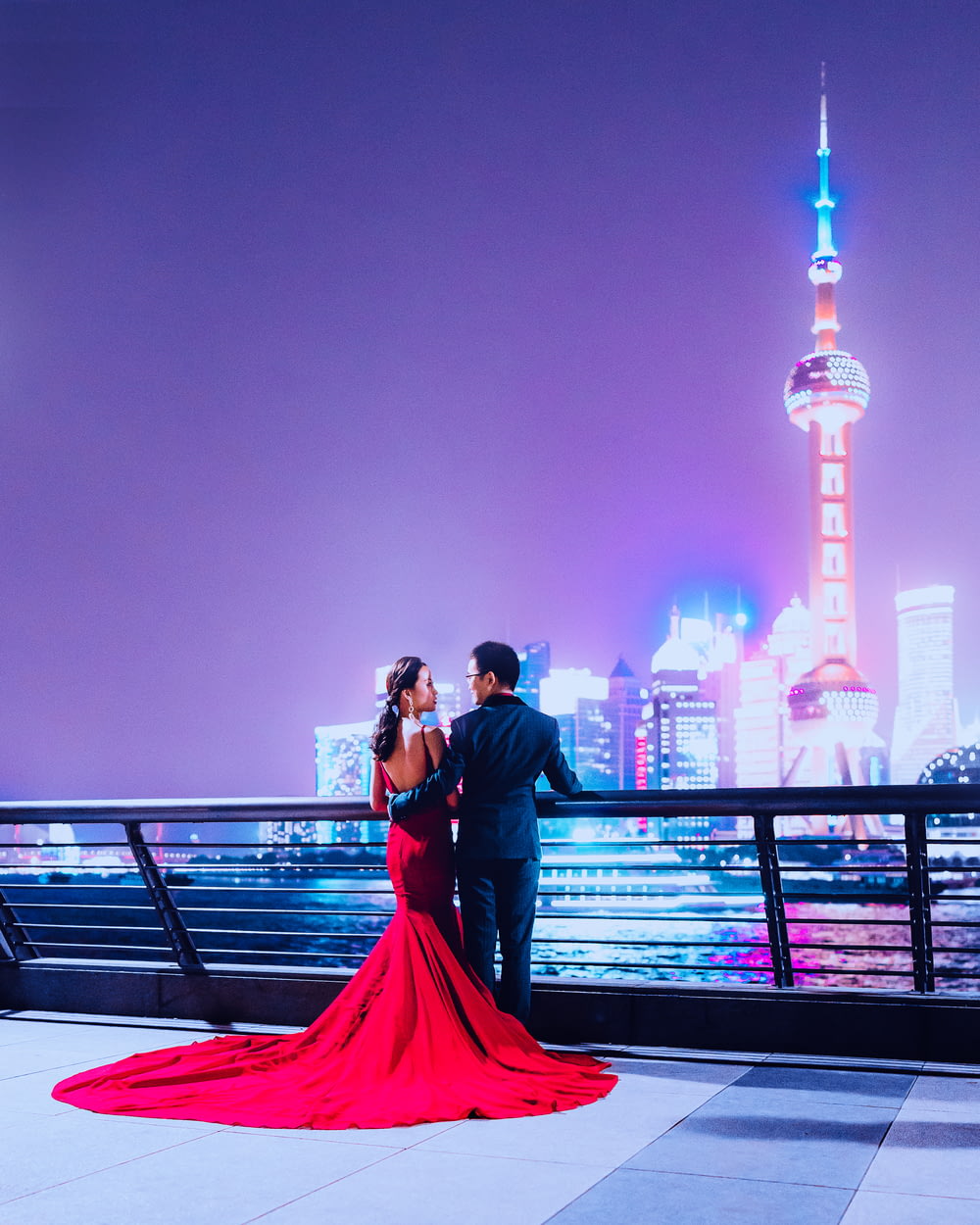 man and woman standing beside rail facing on Oriental Pearl Tower during nighttime