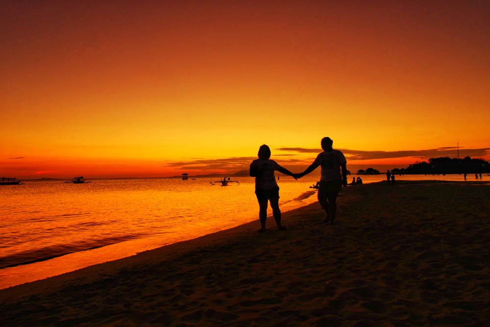 man and woman walking hand in hand in beach at sunset