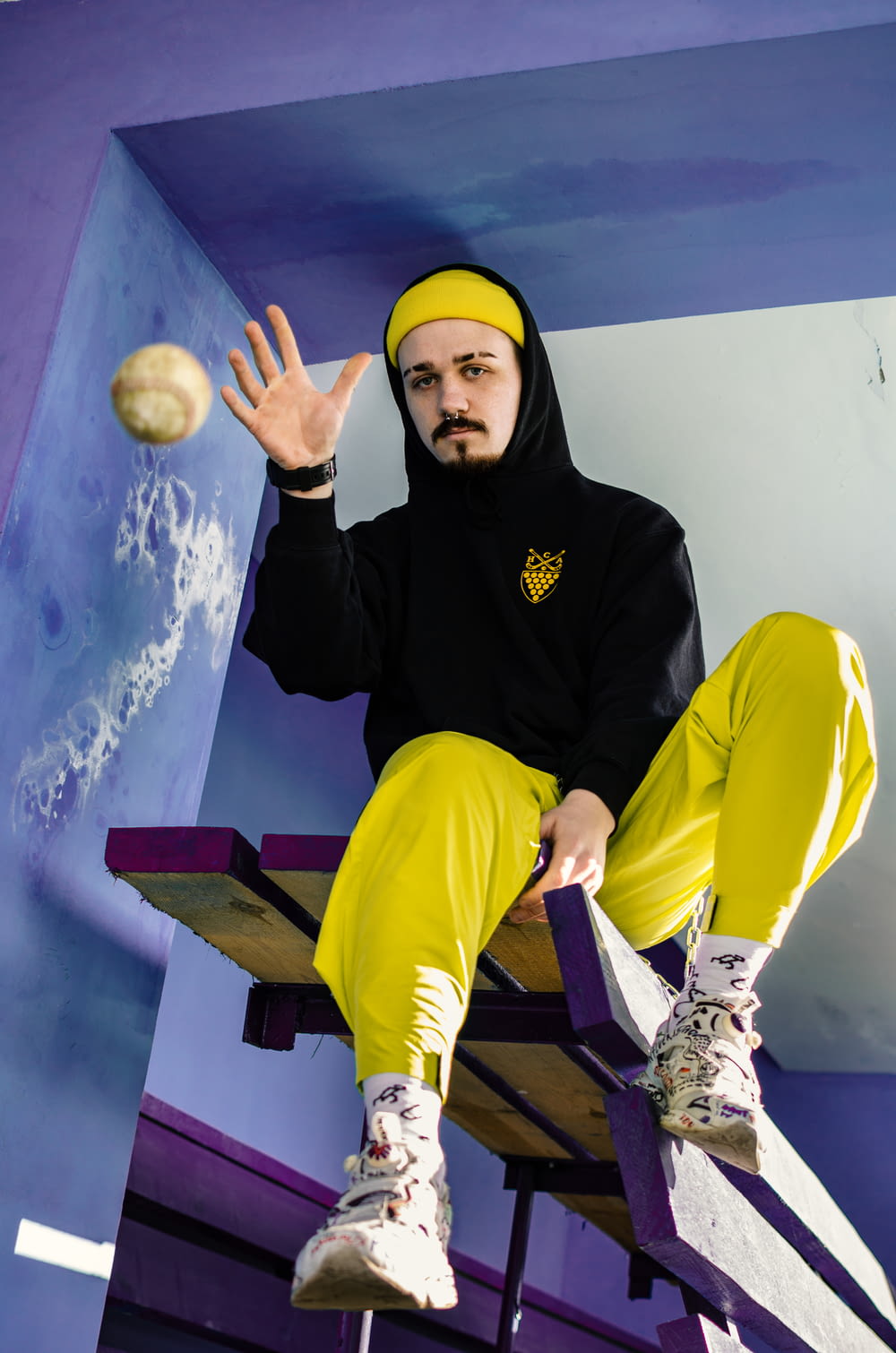 man wearing yellow pants and black hoodie about to throw the tennis ball