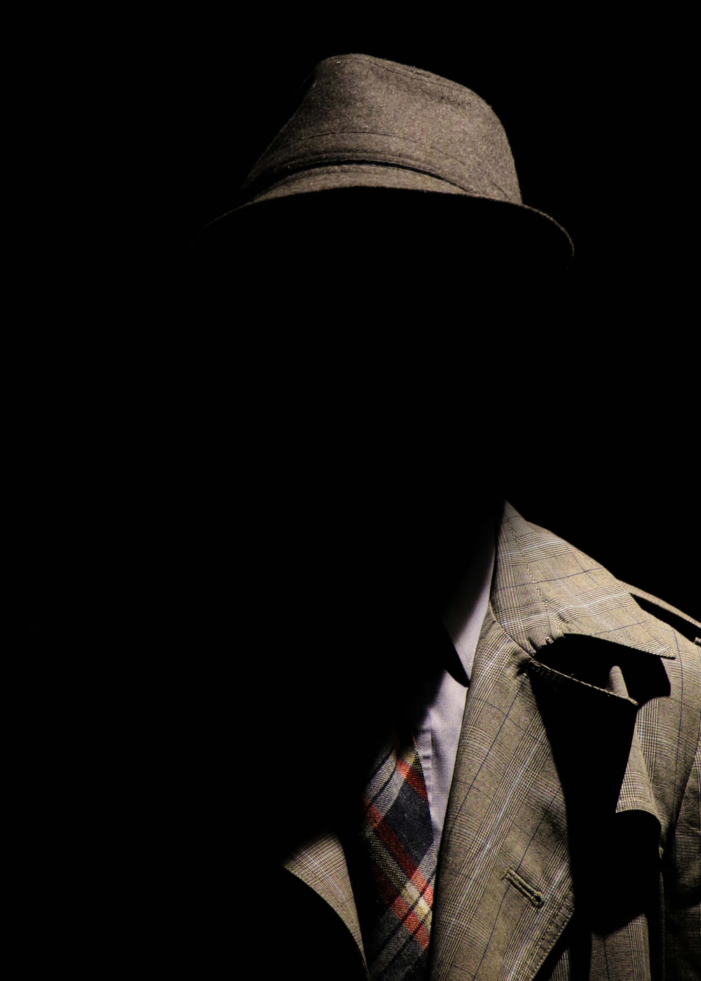 灰色のチェック柄のノッチ付きラペルスーツジャケットと灰色の帽子をかぶった人が顔を隠している