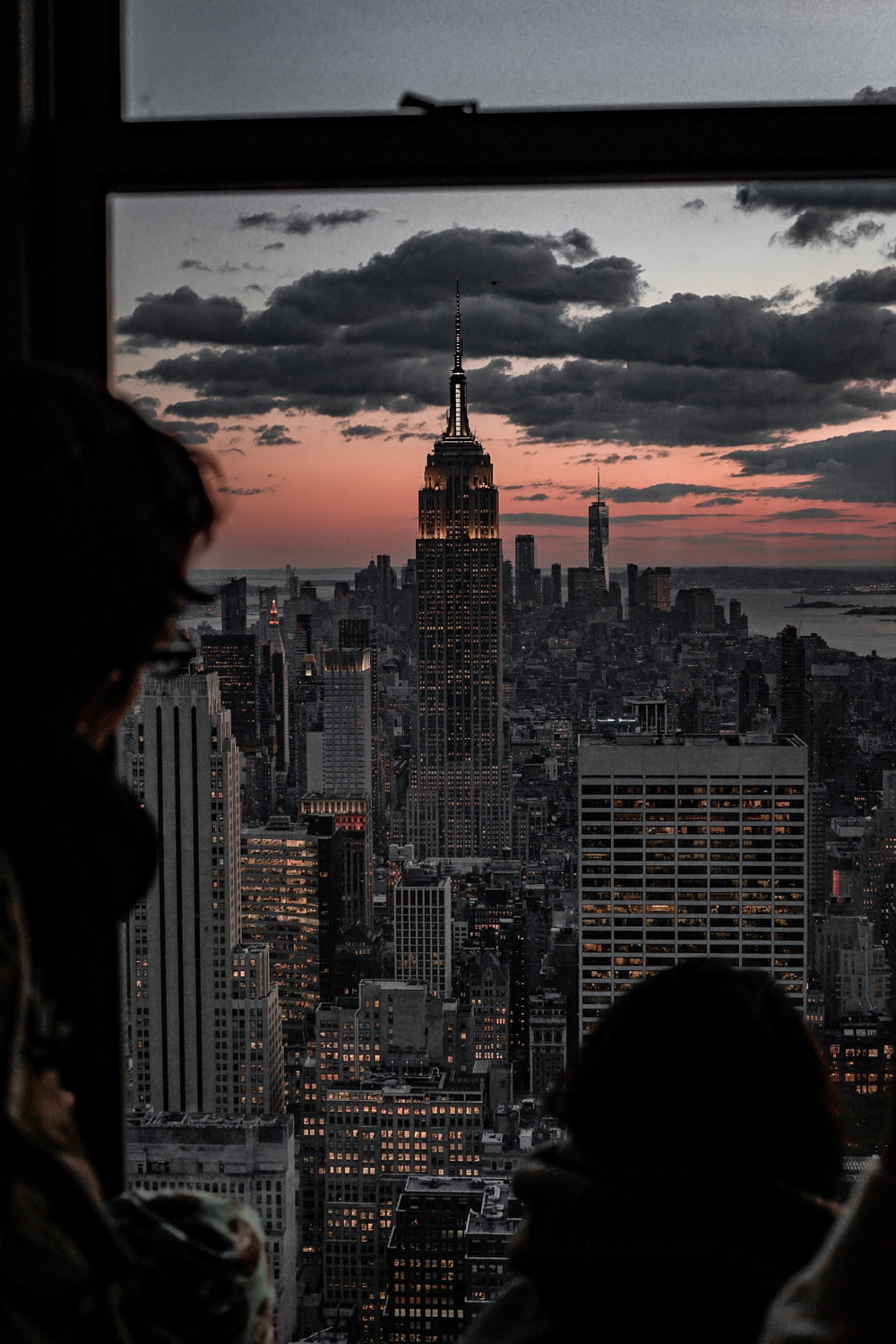 person looking at Empire State Building from glass window at dusk