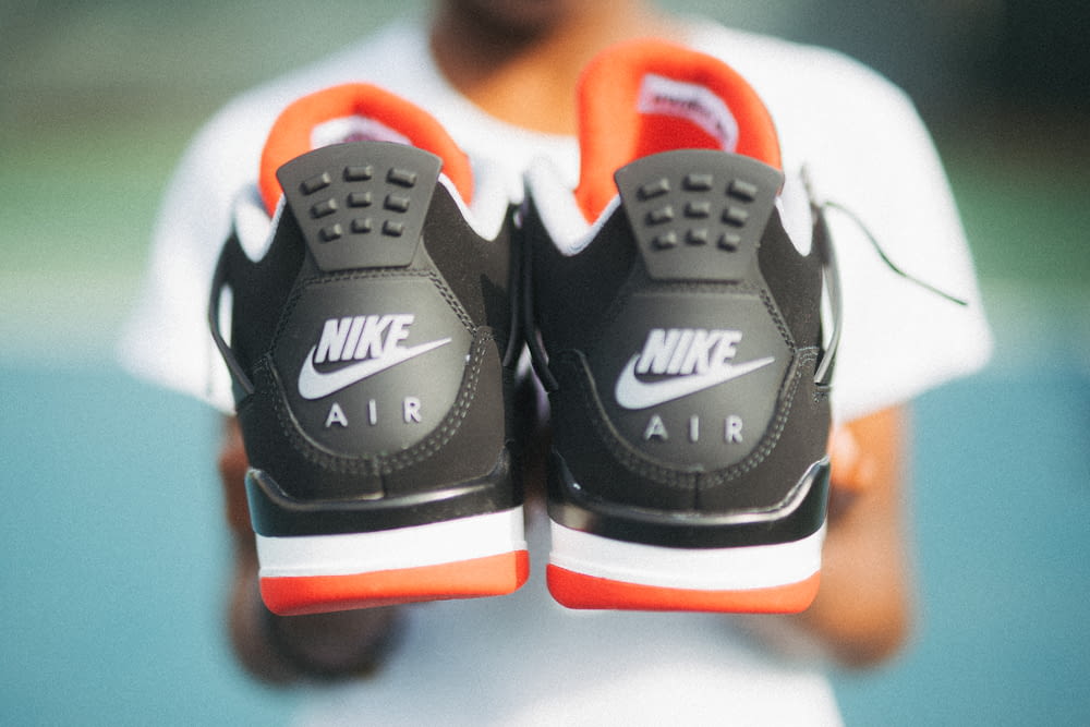 Junge hält ein Paar schwarz-orangefarbene Nike Air-Schuhe in der Hand