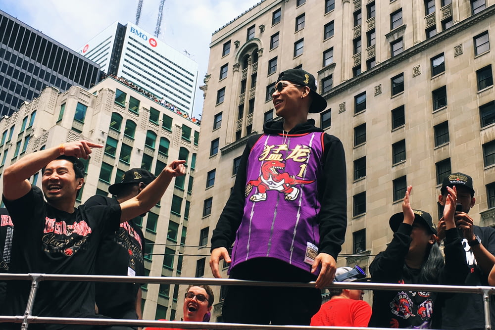 smiling \Jeremy Lin in Raptor uniform atop of vehicle by men during daytime