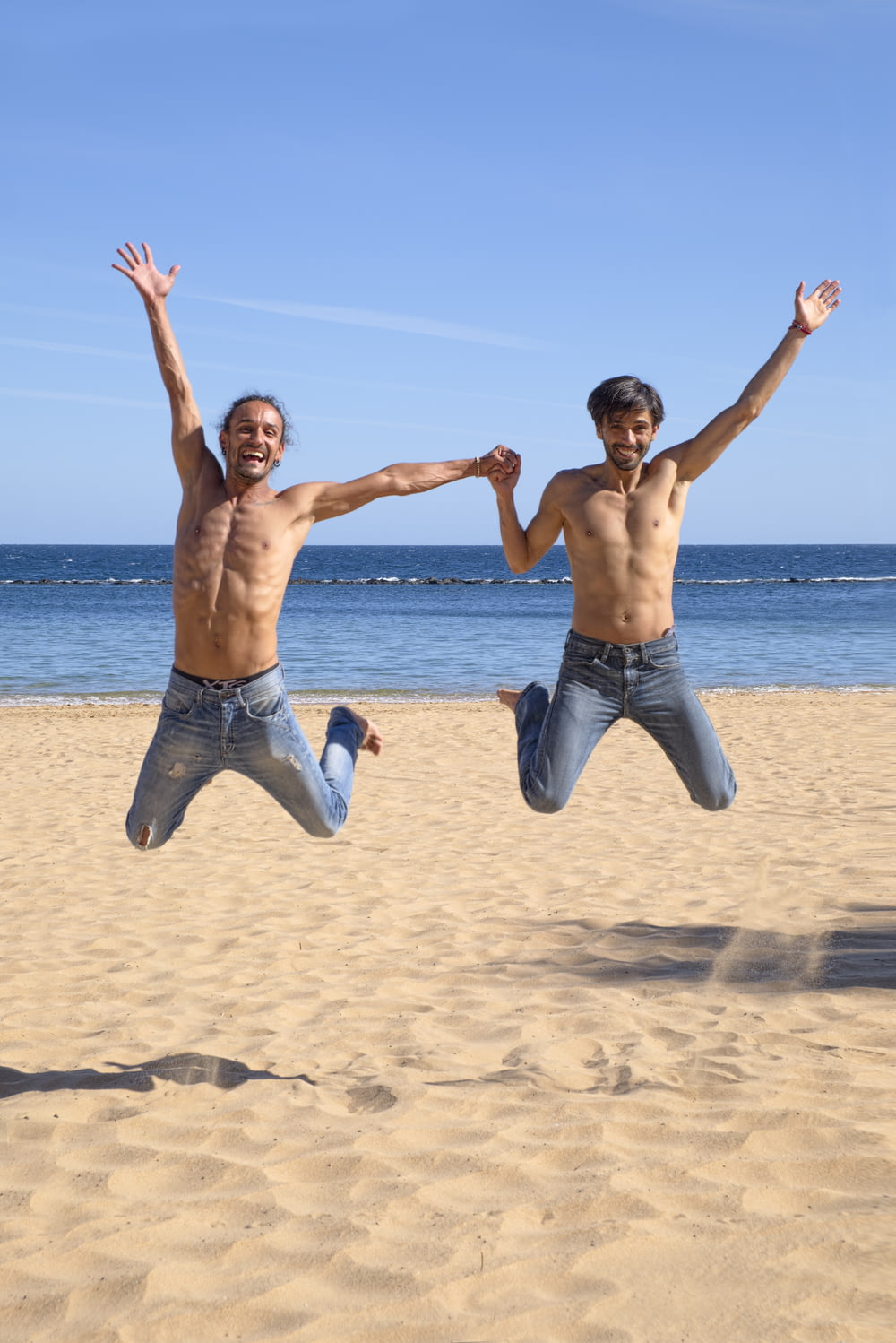 Dois homens pulando sobre a areia marrom da praia