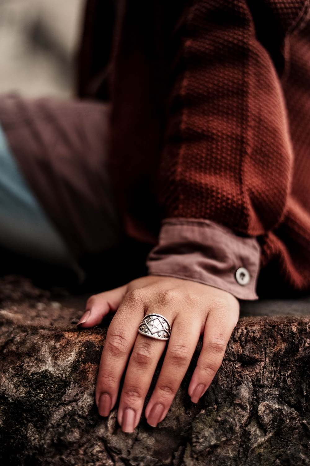 person sitting on brown tree trunk wearing silver-colored ring close-up photography