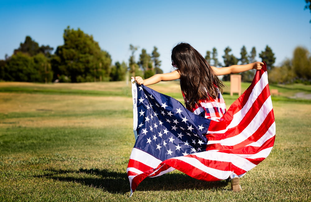 niña sosteniendo la bandera de EE.UU. en la pradera