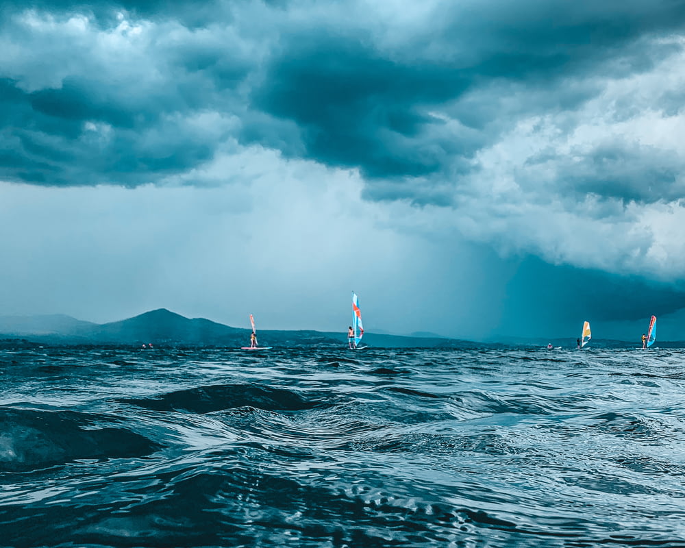 a group of sailboats in the ocean under a cloudy sky