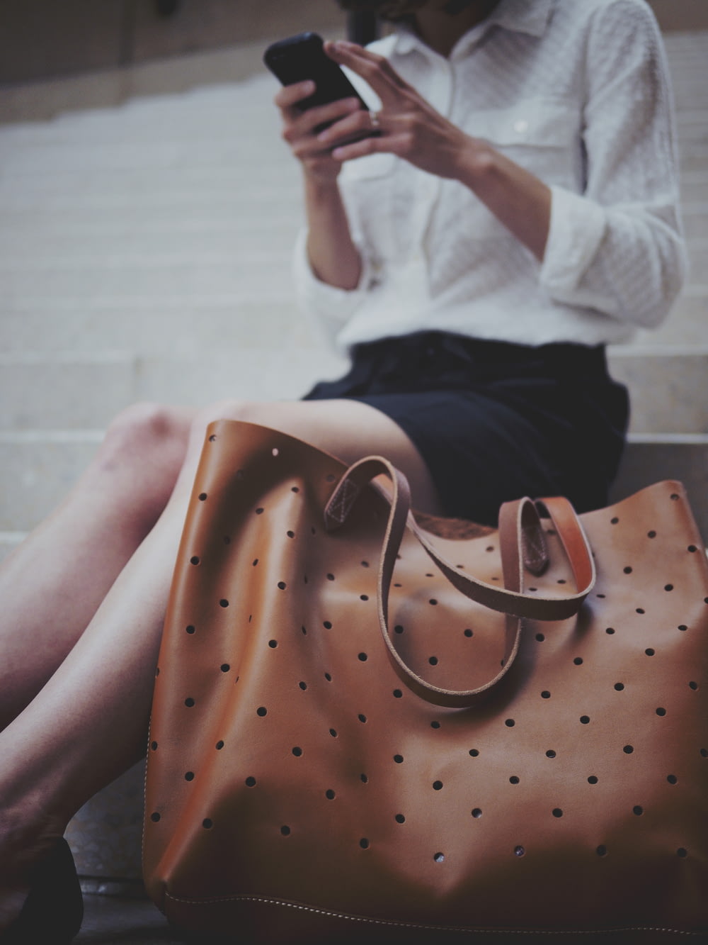 Frau sitzt auf Betontreppe neben brauner Ledertragetasche
