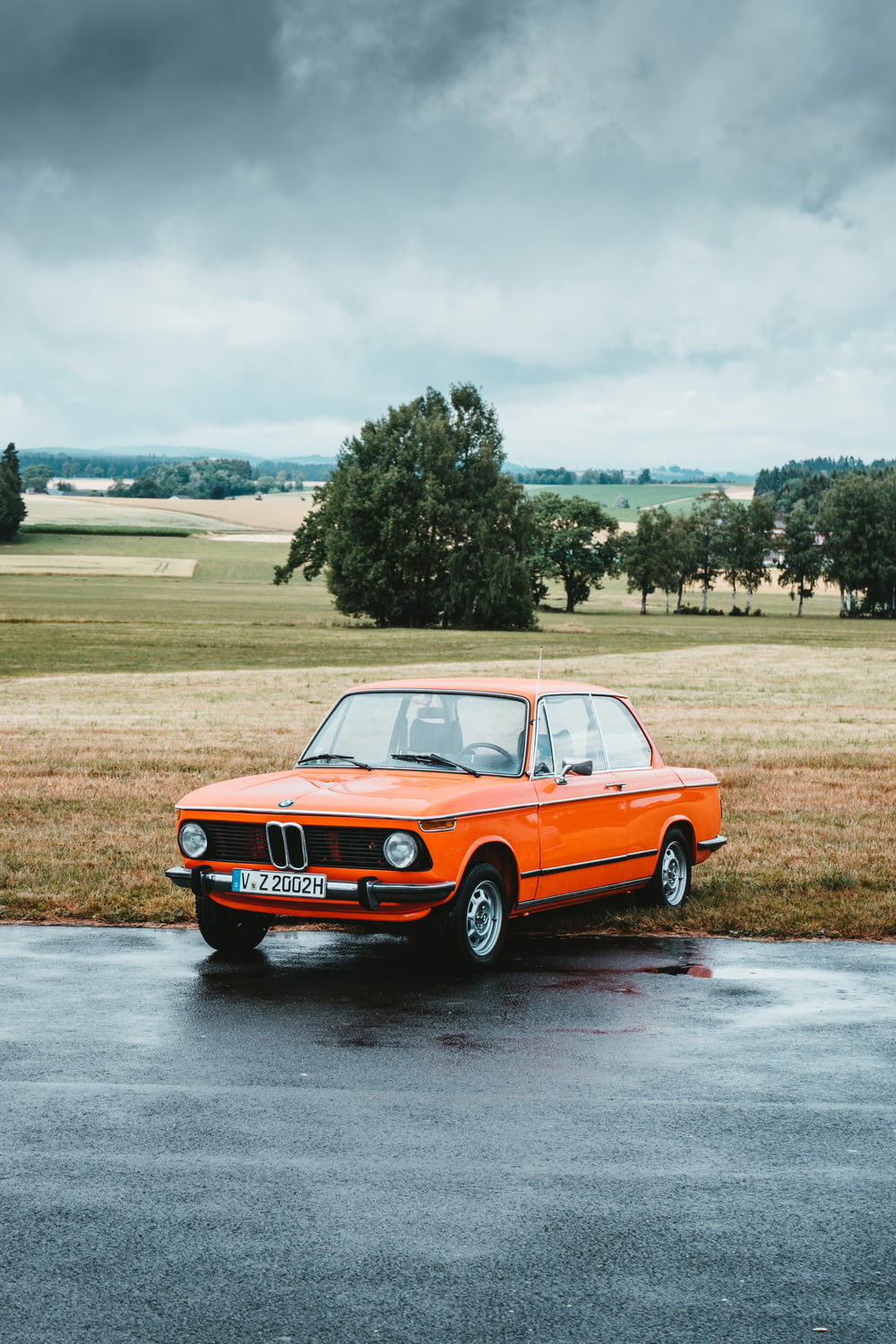 BMW coupé clásico naranja estacionado al borde de la carretera bajo un cielo gris nublado
