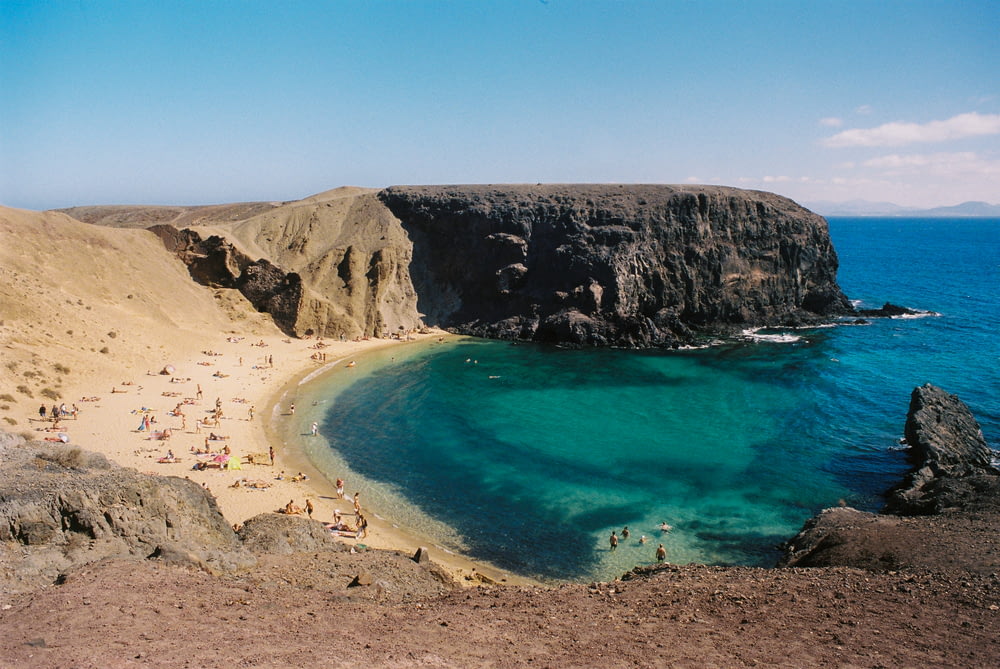 une plage de sable avec une eau bleue claire à côté d’une falaise