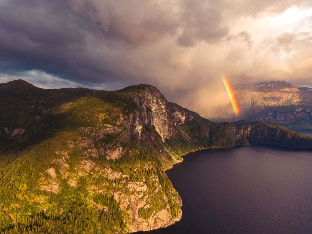 Cuerpo de agua cerca de la montaña con arco iris durante el día