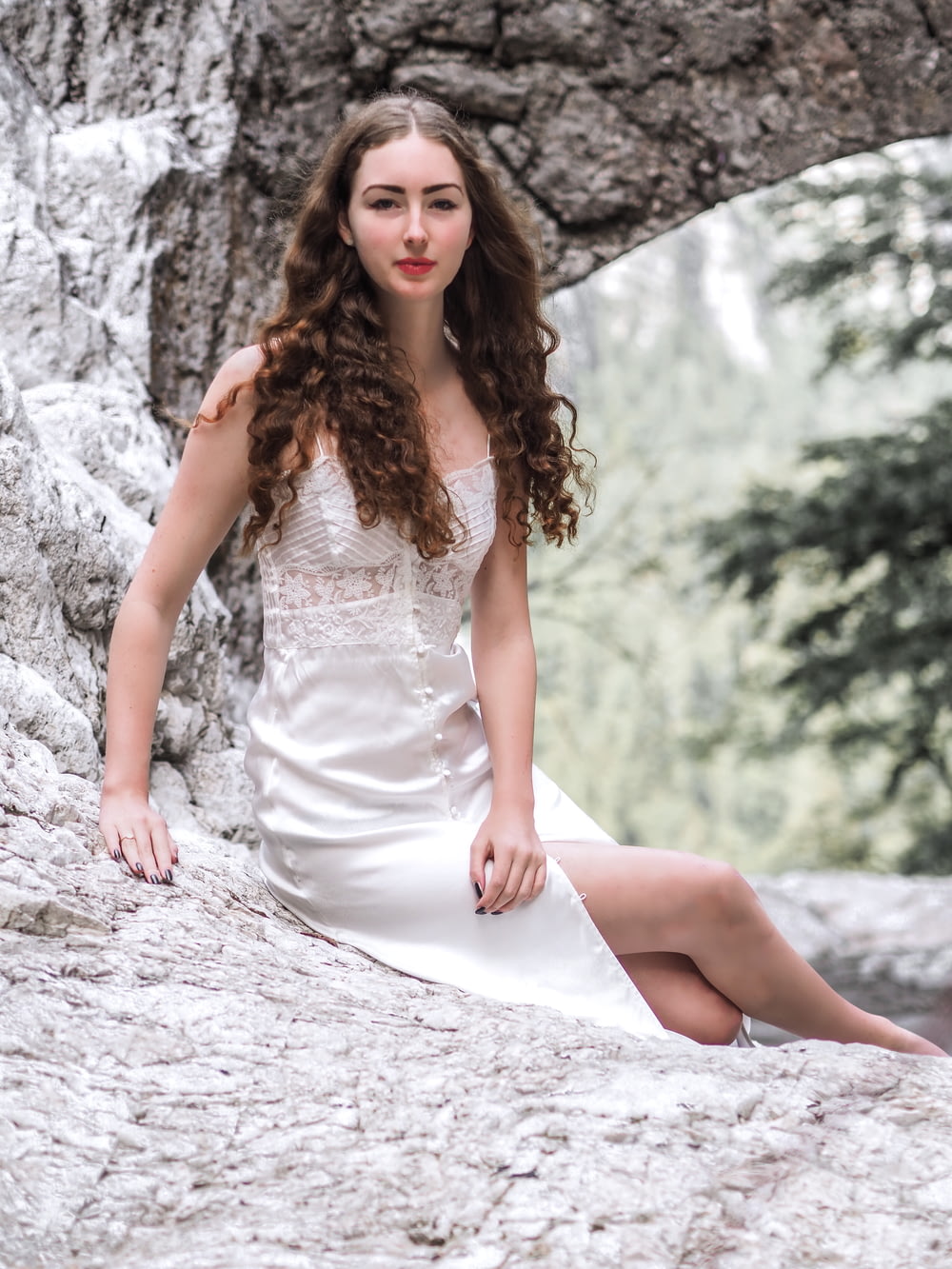 smiling woman in white button-up dress sitting on rock