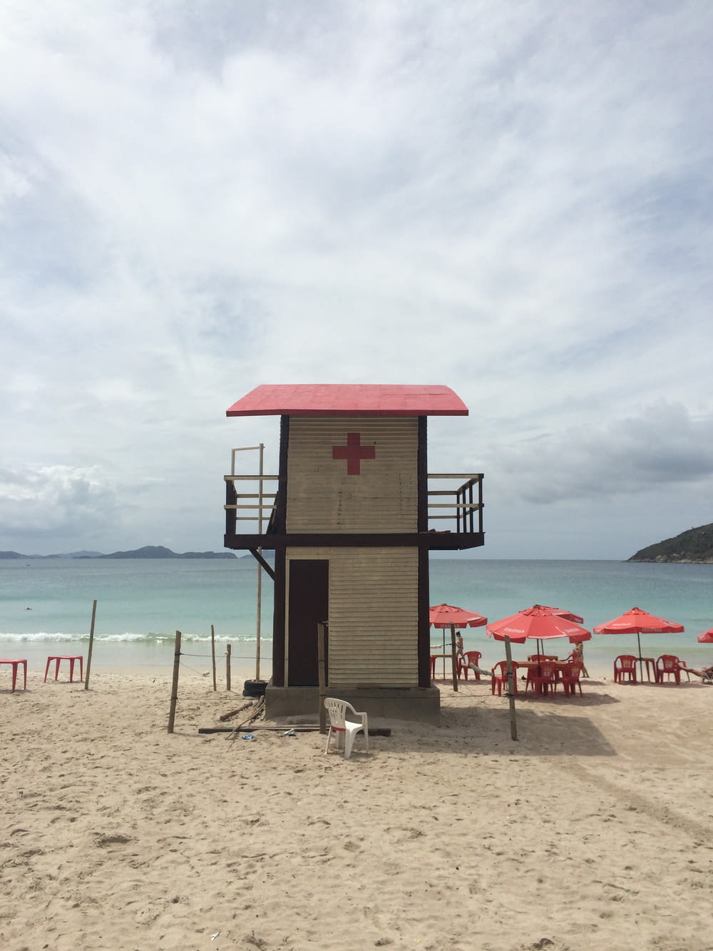white and red lifeguard house near red beach chairs under white skies