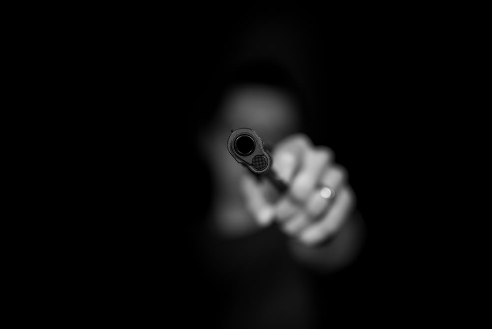 Photographie en niveaux de gris d’une personne tenant une arme à feu
