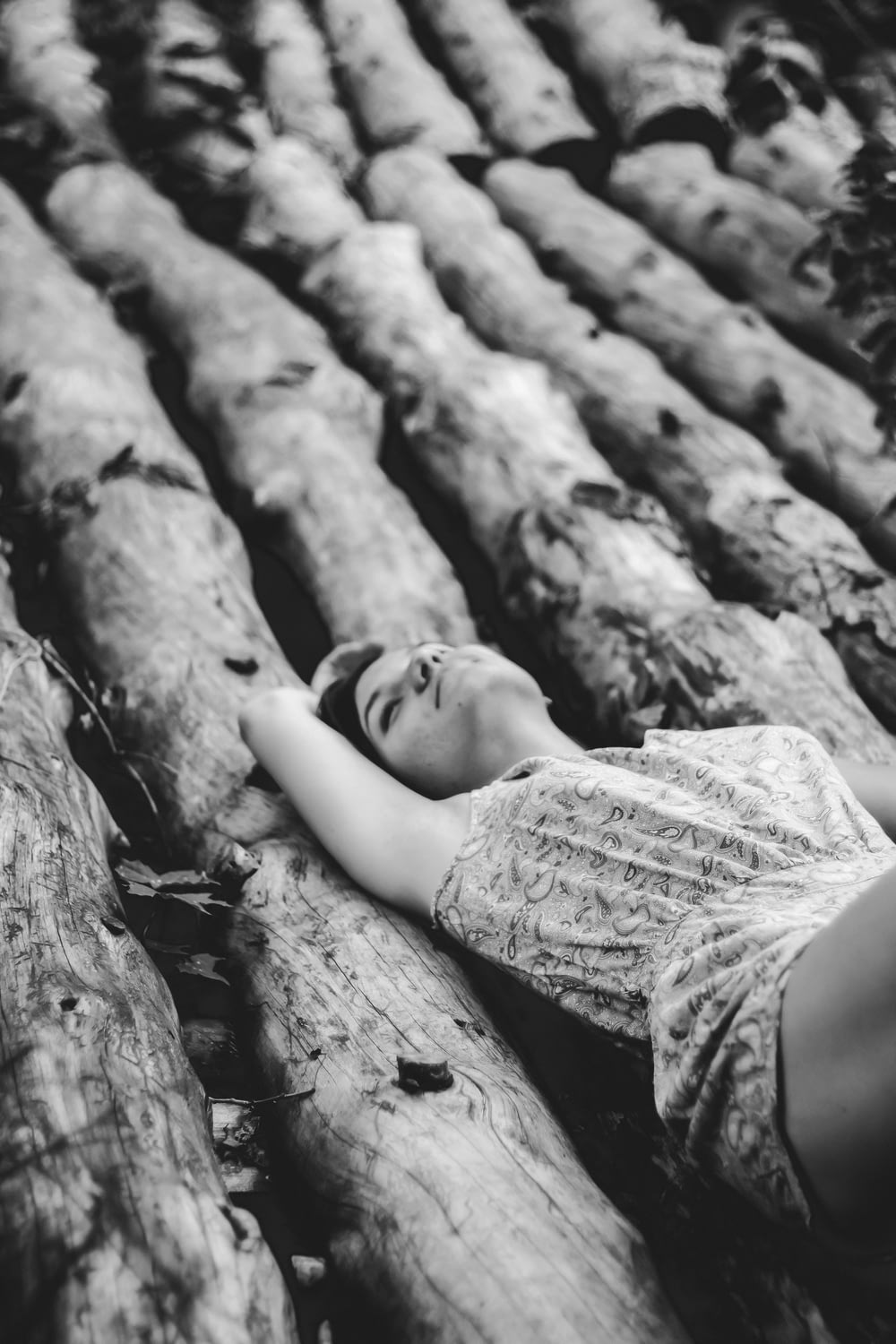 grayscale photo of a woman on tree trunks