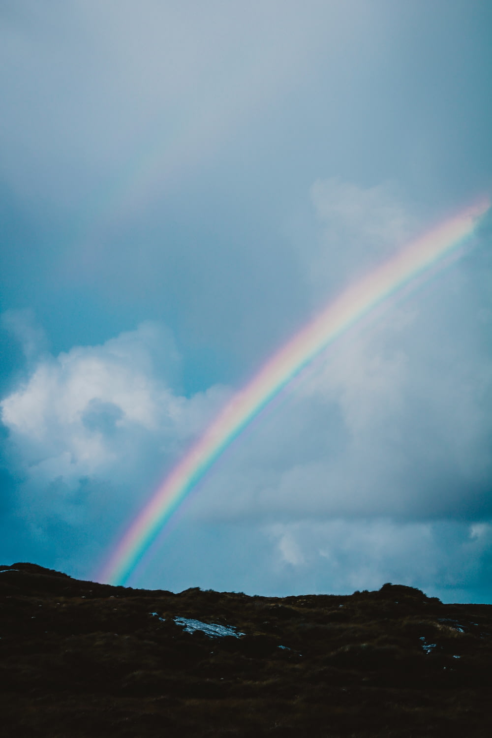a rainbow appears in the sky above a hill