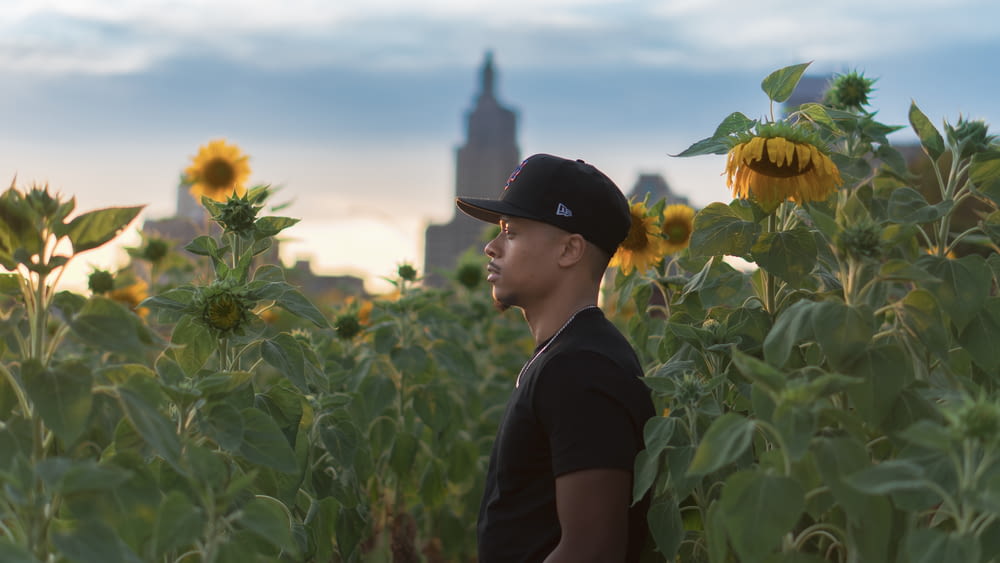 man standing surrounded with sunflowers during daytime