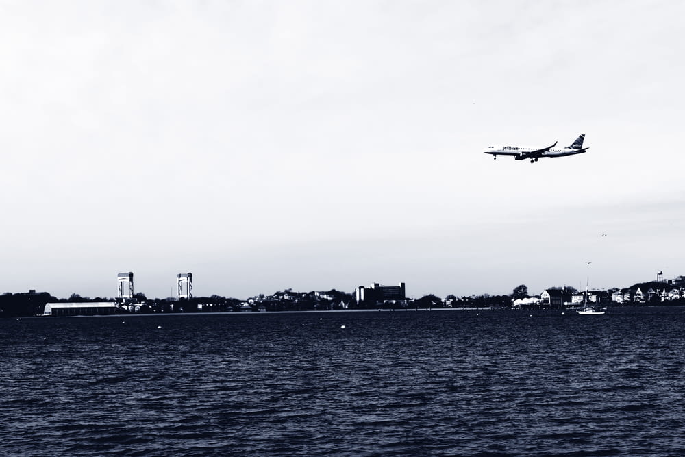 grayscale photography of airplane above sea viewing buildings